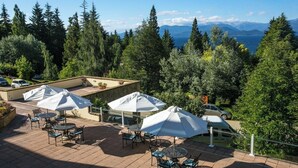 An outdoor patio with multiple tables and umbrellas, surrounded by dense trees and a view of mountains and a lake. - 2 Mountain Getaways w/ Breakfast, Indoor Pool & Near Civic Center (San Carlos de Bariloche)