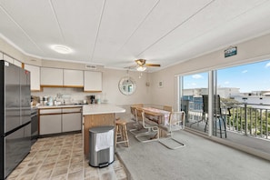 A modern kitchen with a dining area, a balcony with a view, and a ceiling fan. - Salty Sands 404- 02 |Steps to Ocean & Dining (Ocean City)