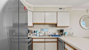 A kitchen with white cabinets, a stainless steel refrigerator, and a blue countertop. - Salty Sands 404- 02 |Steps to Ocean & Dining (Ocean City)