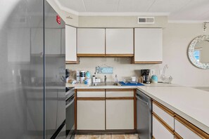 A kitchen with white cabinets, a stainless steel refrigerator, and a blue countertop. - Salty Sands 404- 02 |Steps to Ocean & Dining (Ocean City)
