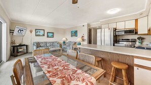 A modern kitchen with a refrigerator, microwave, and stove. There is a dining area with a table and chairs. - Salty Sands 404- 02 |Steps to Ocean & Dining (Ocean City)