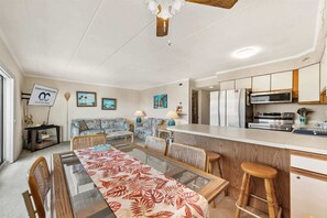 A modern kitchen with a refrigerator, microwave, and stove. There is a dining area with a table and chairs. - Salty Sands 404- 02 |Steps to Ocean & Dining (Ocean City)