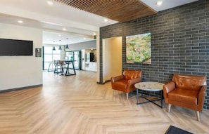A modern interior with a herringbone floor, leather armchairs, a round table, a brick wall with a map, and a visible kitchen area. - Extended Stay Suites | 2 Units | Fort Myers Location + Breakfast Included (Fort Myers)
