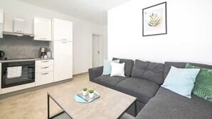 Eine moderne Küche mit weißen Schränken, einer Kaffeemaschine und einem Essbereich mit grauem Sofa und Couchtisch.