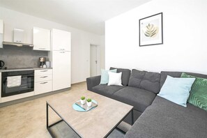 Eine moderne Küche mit weißen Schränken, einer Kaffeemaschine und einem Essbereich mit grauem Sofa und Couchtisch.