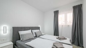 Ein Zweibettzimmer mit grauem Kopfteil, weißer Bettwäsche und grauen Vorhängen.