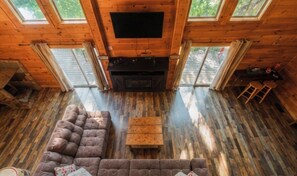 A wooden cabin interior with a fireplace, a sofa, and a television.
