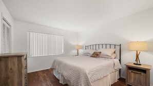 Ein Schlafzimmer mit einem Bett, Nachttischen, einem Fenster mit Jalousien und einem Holzboden.