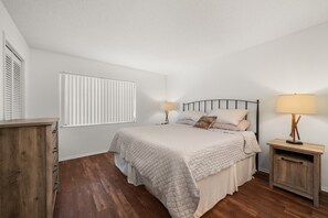 Een slaapkamer met een bed, nachtkastjes, een raam met zonwering en een houten vloer.