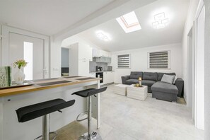 A modern kitchen with a bar area, a grey sofa, and a dining table. - Gasparevic Apartment 5 (Rovinj)