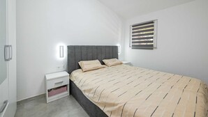 A bedroom with a bed, bedside tables, a window with blinds, and a wall-mounted light fixture. - Gasparevic Apartment 5 (Rovinj)