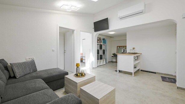 A modern living room with a grey sectional sofa, a small wooden coffee table, and a TV mounted on the wall. - Gasparevic Apartment 5 (Rovinj)