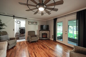 A living room with hardwood flooring, a fireplace, a ceiling fan, and a view of the backyard through glass doors. - Gorgeous 3 Bed 1.5 Bath House in Premium location (Springfield)