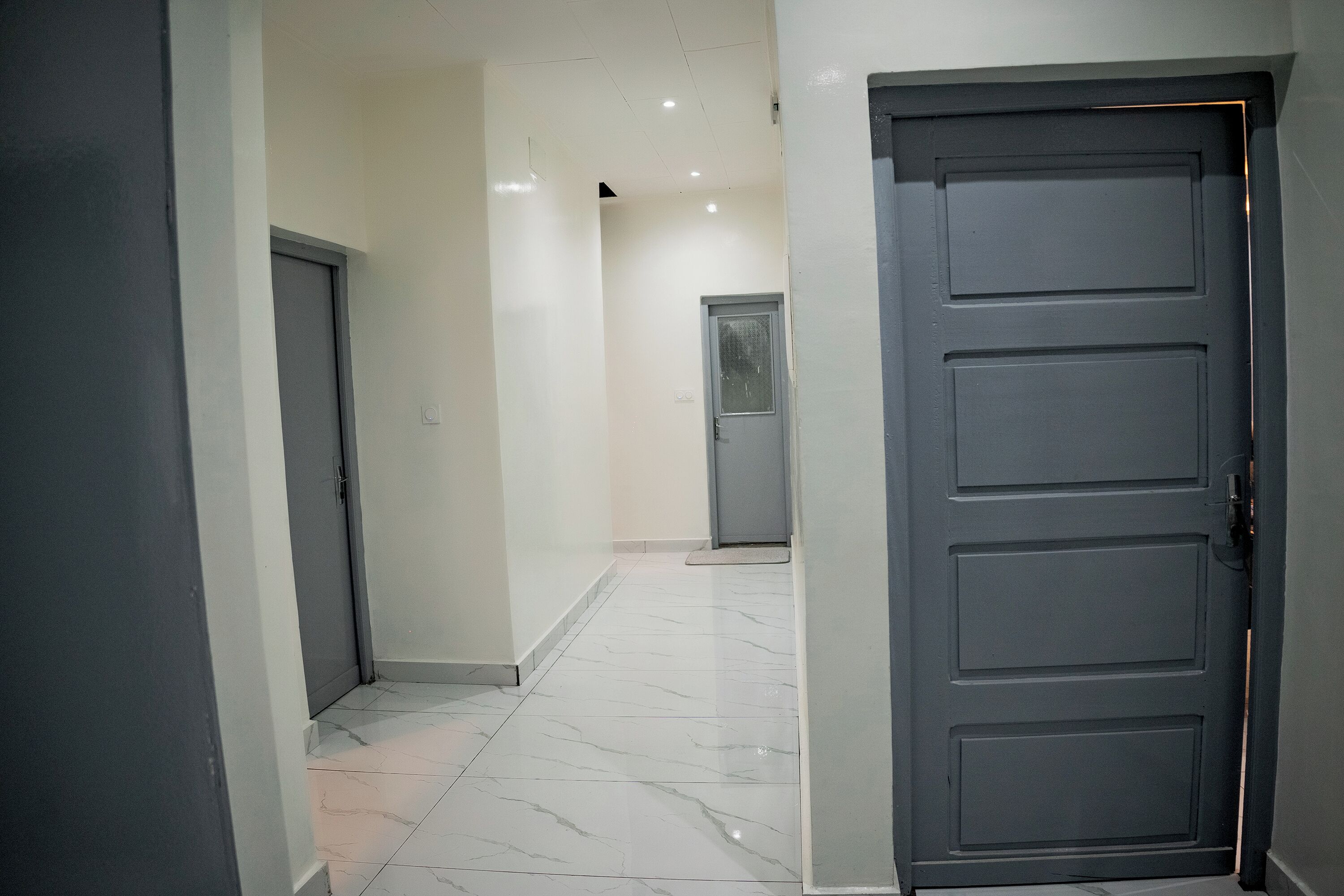 Um corredor com chão de mármore, uma porta fechada e um interruptor na parede.