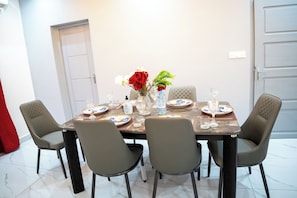 A dining table set for four with chairs, a vase with flowers, and plates with blue and white designs. - Appartement Chic Bastos - High Security, Air Conditioning, Wifi (Yaoundé)