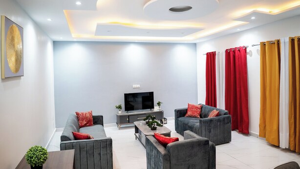 Ein modernes Wohnzimmer mit Flachbildfernseher, grauen Sofas, roten Kissen, einem Couchtisch und einer Decke mit Einbauleuchten.