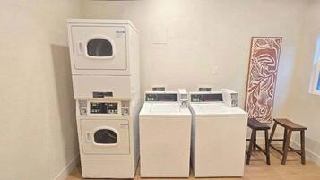 Een wasserette met gestapelde wasmachines en drogers, een houten kruk en een decoratief wandobject.