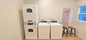 Een wasserette met gestapelde wasmachines en drogers, een houten kruk en een decoratief wandobject.