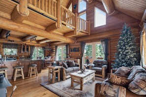 Ein Blockhaus-Interieur mit einer Holztreppe, einer Essecke, einem Wohnzimmer mit Sofas und einem Couchtisch sowie einem Weihnachtsbaum.