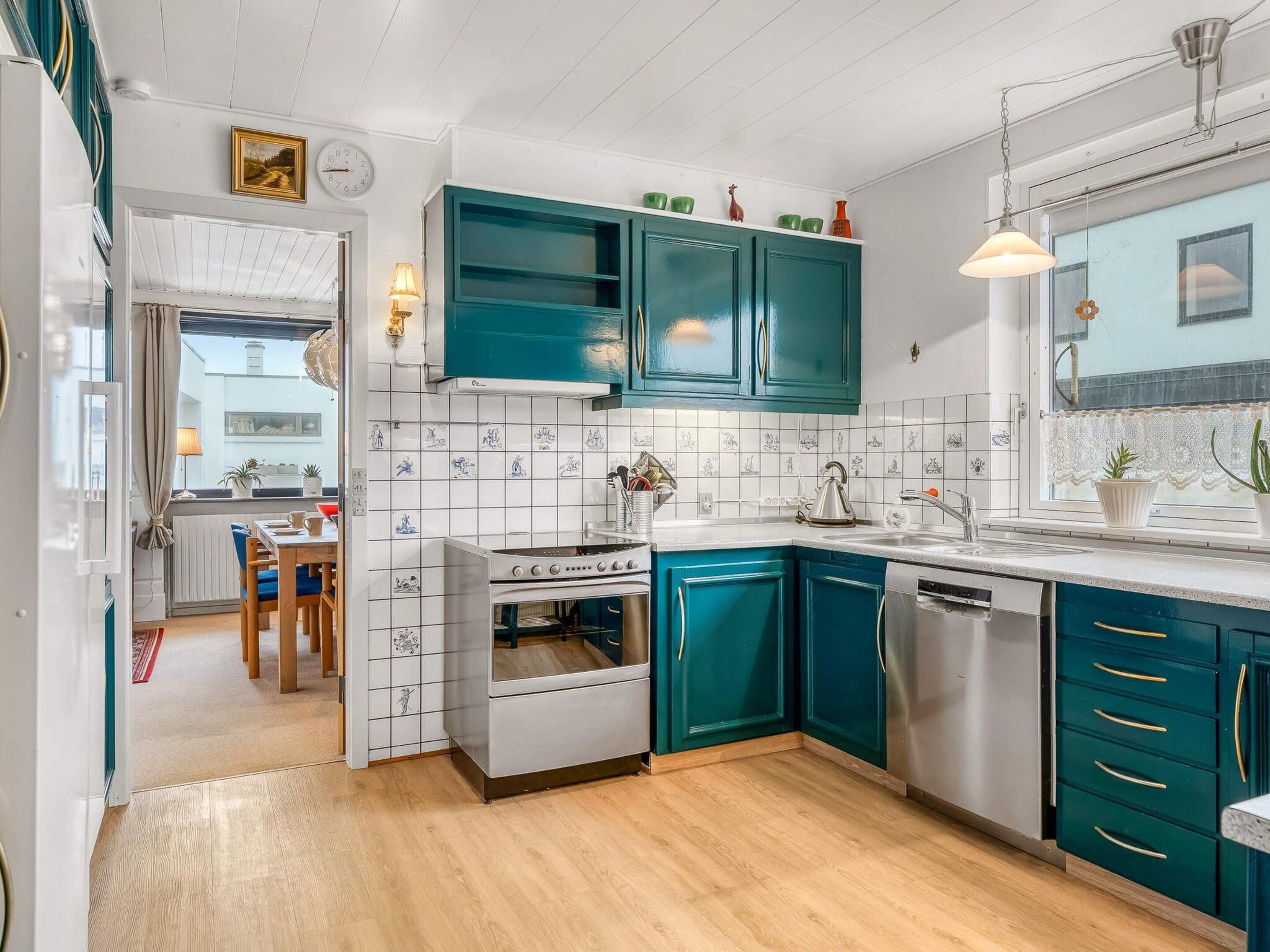A compact kitchen with teal cabinets, a white stove, and a window with a view.