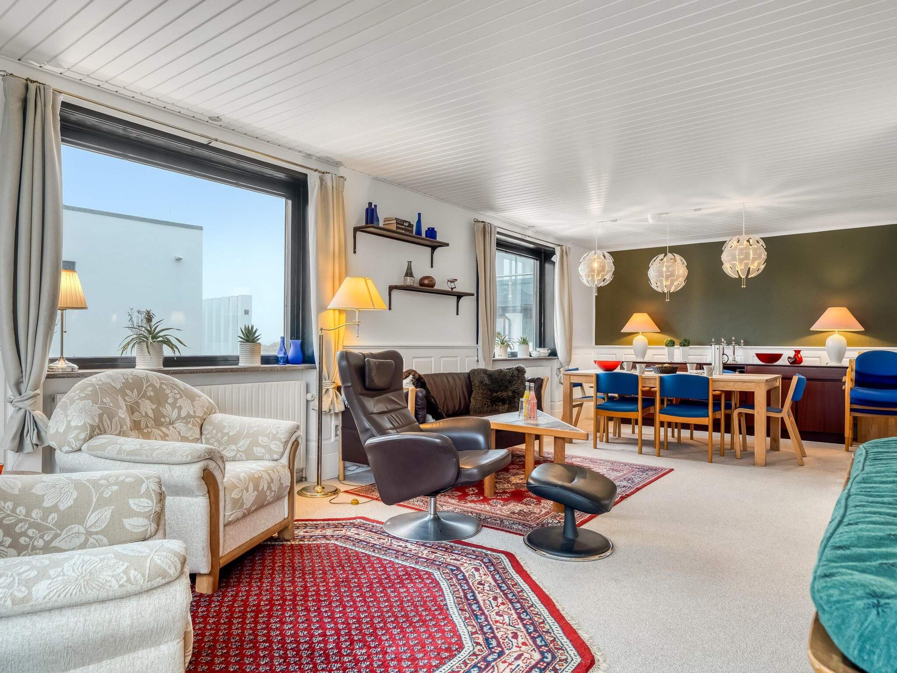 Un salon moderne comprenant un canapé, un fauteuil et un coin repas avec des chaises et une table.