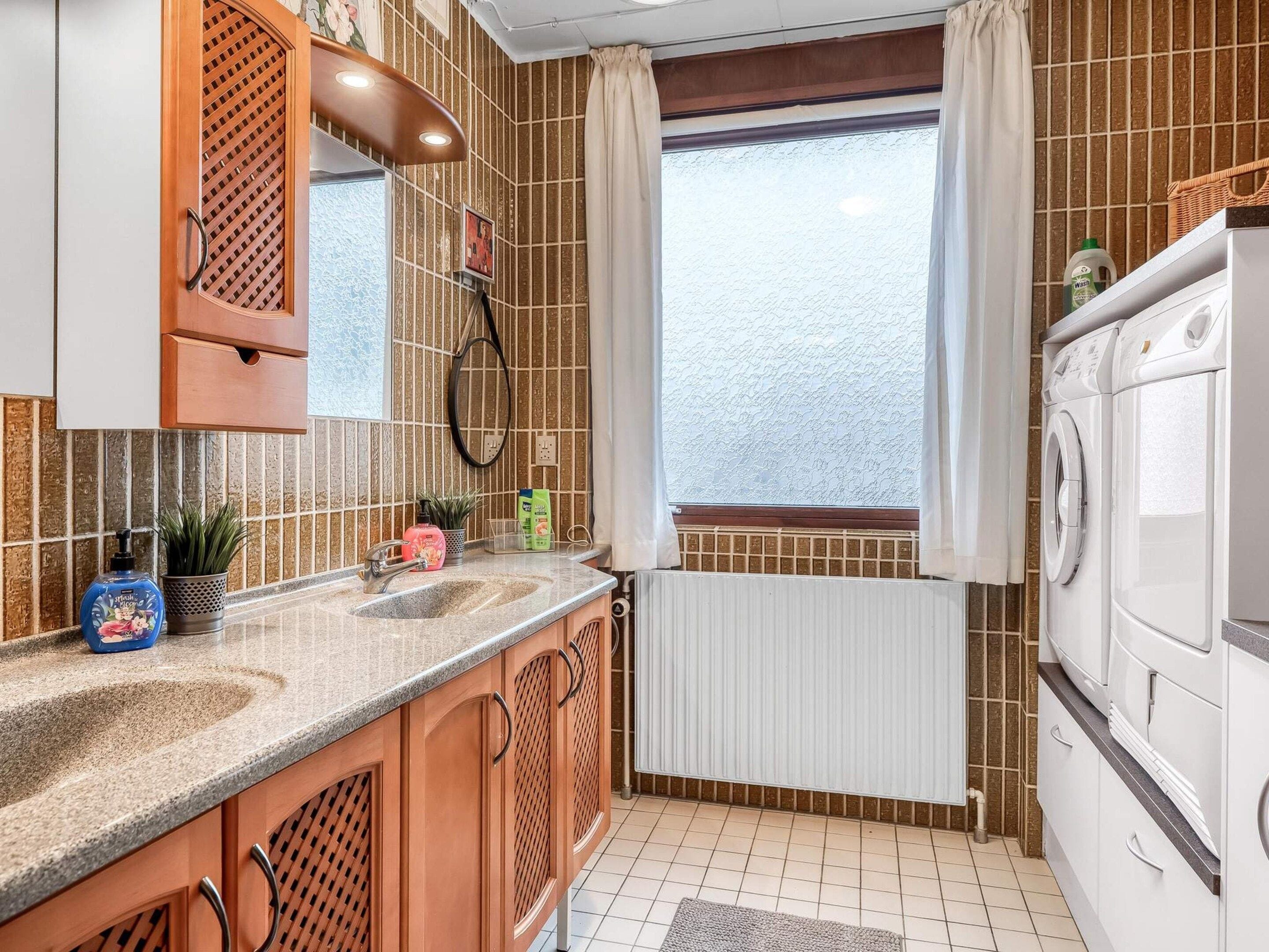 A kitchen with a double sink, wooden cabinets, a built-in oven, and a window with curtains.