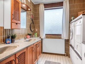 Eine Küche mit einem doppelten Waschbecken, Holzschränken, einem eingebauten Backofen und einem Fenster mit Vorhängen.