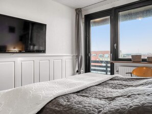 Ein Schlafzimmer mit einem Bett, einem Fernseher, einem Fenster mit Vorhängen und Blick auf Gebäude.