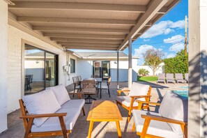 An outdoor patio with a wooden table and chairs, a sofa, and a pool area with lounge chairs. - Arcadia 5BR Oasis, Pool, Putting Green & Sleeps 12 (Phoenix)