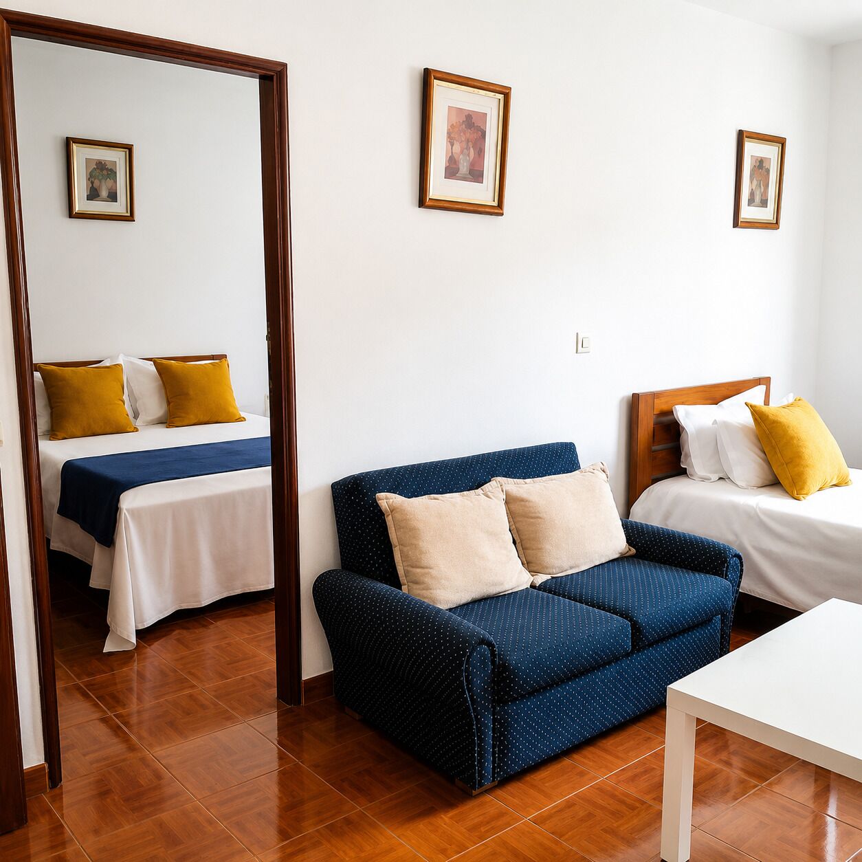 A hotel room with a bed, a blue sofa, a white table, and a mirror reflecting the room.