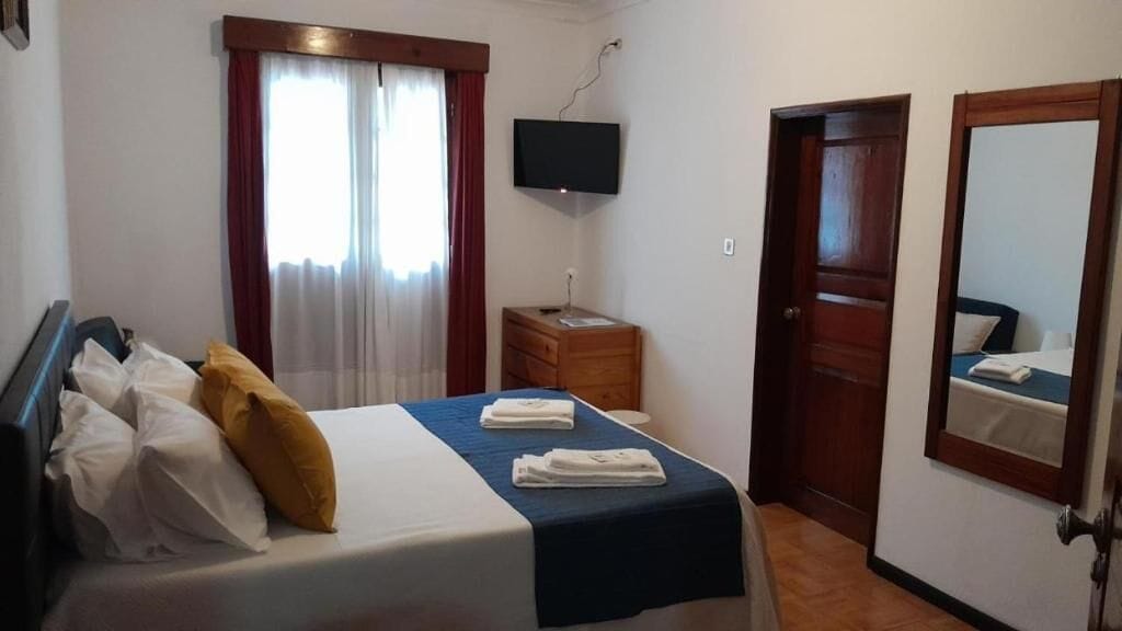 A hotel room with a bed, a television, a wooden dresser, a mirror, and a door.