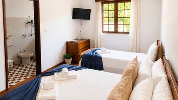 A hotel room with a bed, a TV, a window, a mirror, and a bathroom visible through the door.