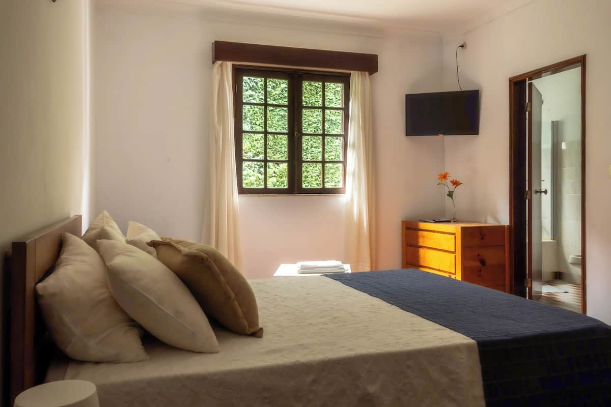 Un dormitorio con cama, cómoda, televisor y ventana con cortinas.