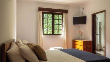 A bedroom with a bed, a dresser, a TV, and a window with curtains.