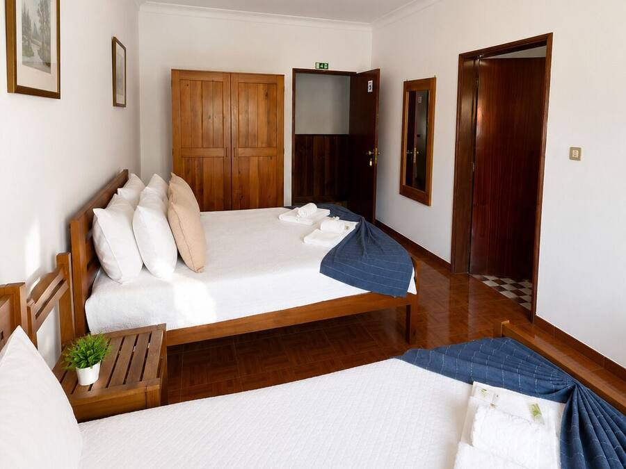 Ein Hotelzimmer mit einem großen Bett, einem Holzschrank, einem kleinen Nachttisch mit Pflanze und einer Tür zu einem weiteren Raum.