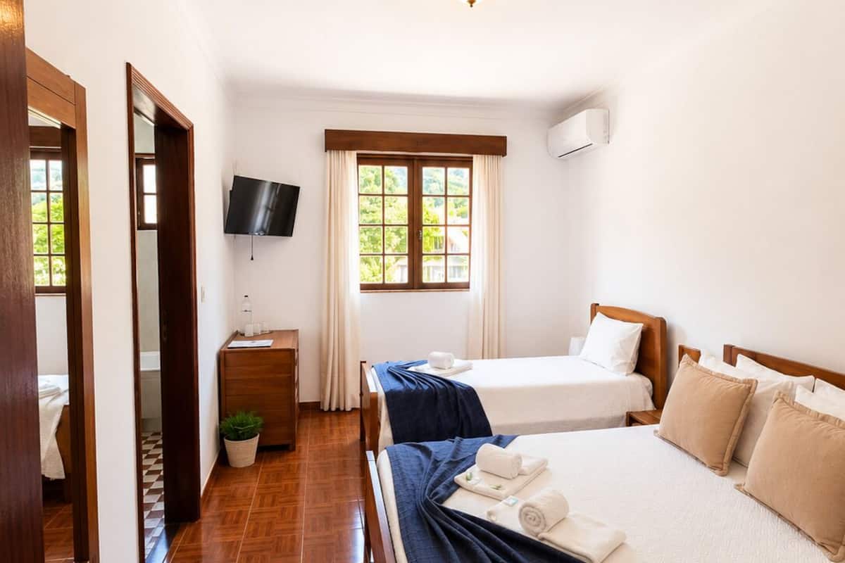Habitación de hotel con dos camas, televisión, ventana con cortinas, suelo de madera y puerta con espejo.
