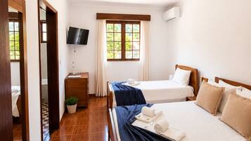 A hotel room with two beds, a TV, a window with curtains, a wooden floor, and a door with a mirror.