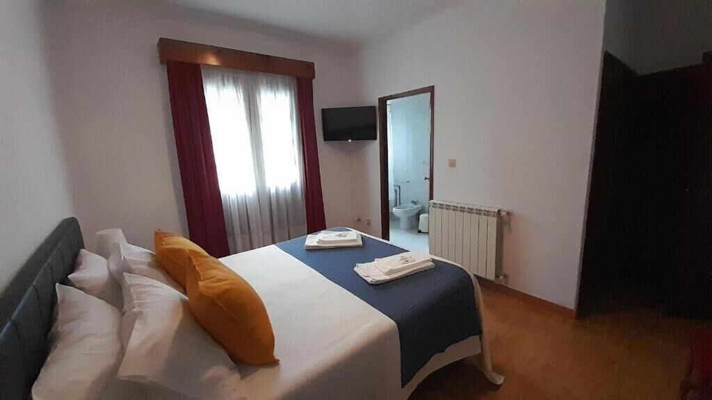 A bedroom with a bed, a TV mounted on the wall, and a door leading to a bathroom.