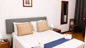 Habitación de hotel con una cama grande, una mesita de noche, un espejo, una silla y un cuadro en la pared.