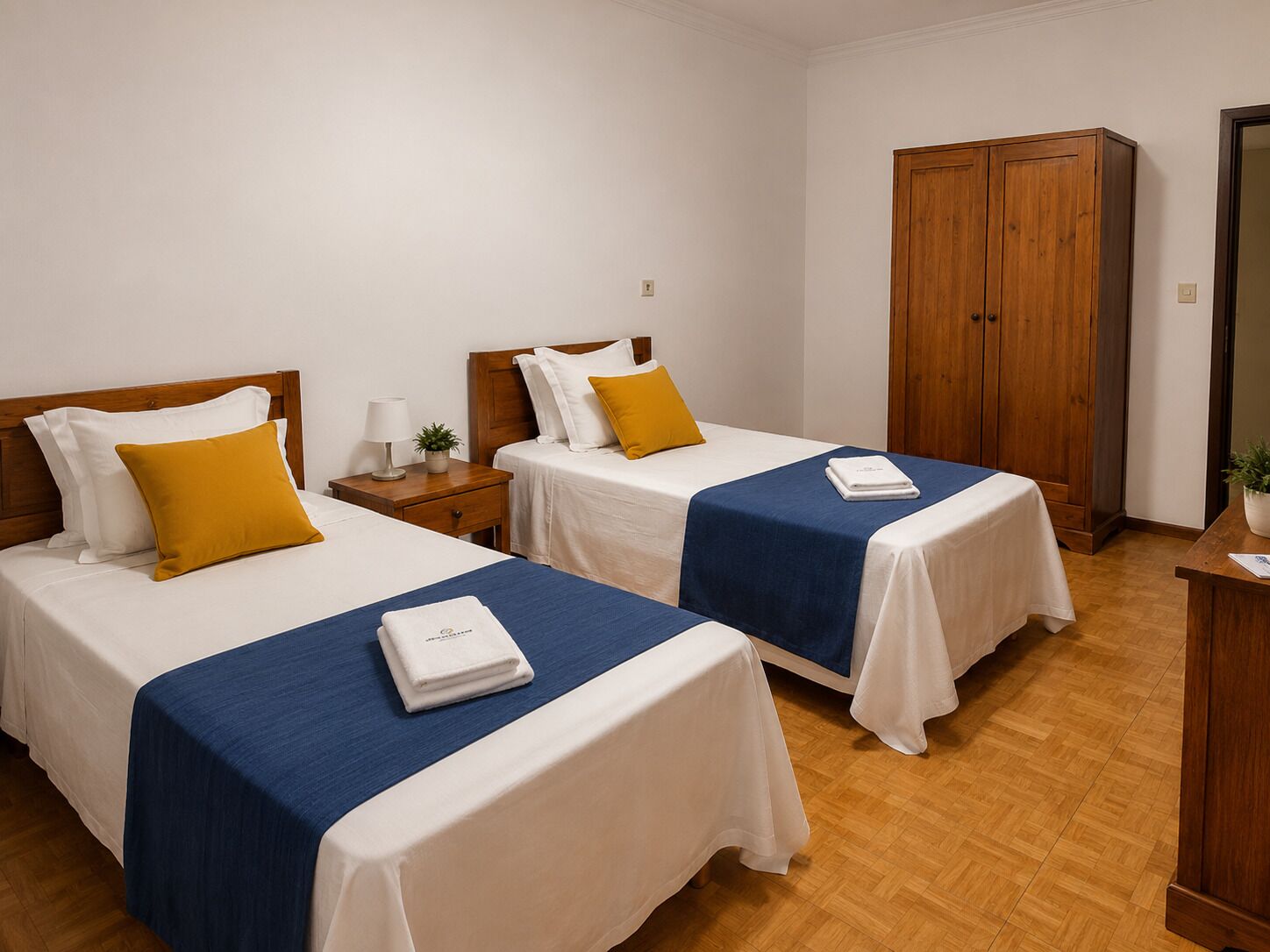 A hotel room with two beds, wooden wardrobe, and a small table with a plant.