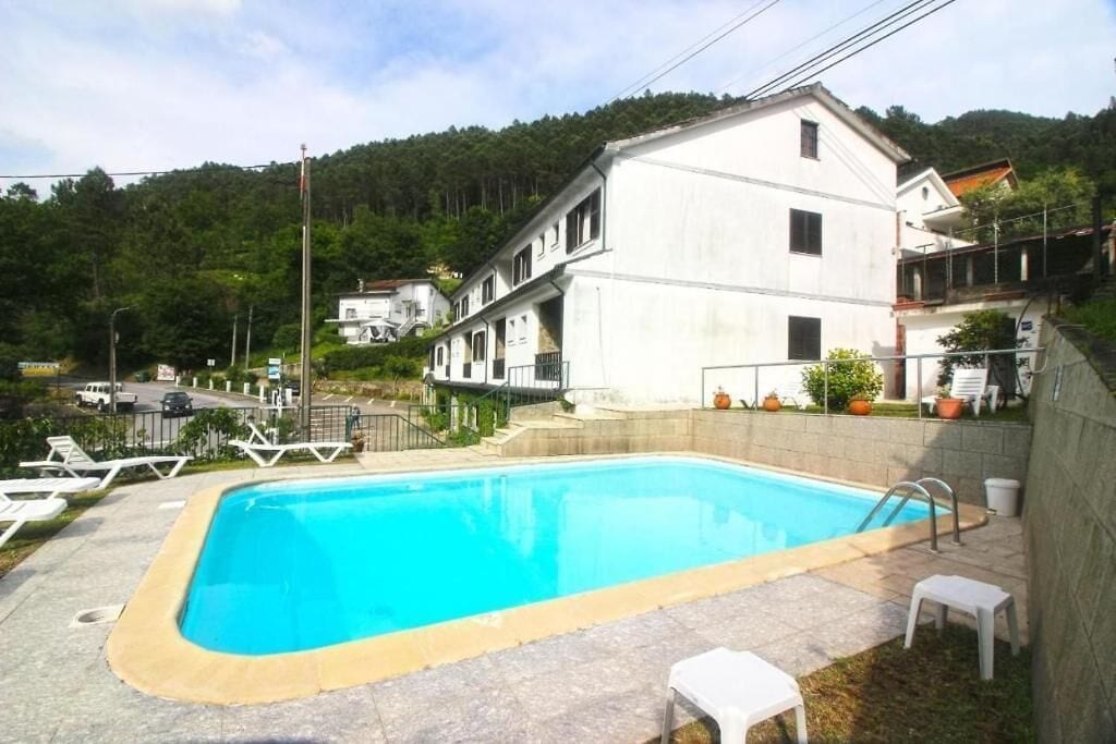 A swimming pool with a clear blue water, surrounded by a stone deck and white lounge chairs.