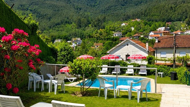 A pool area with lounge chairs, a swimming pool, and a view of a hillside village.