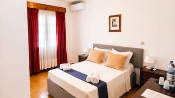 Una habitación de hotel con cama, mesitas de noche, escritorio y ventana con cortinas.