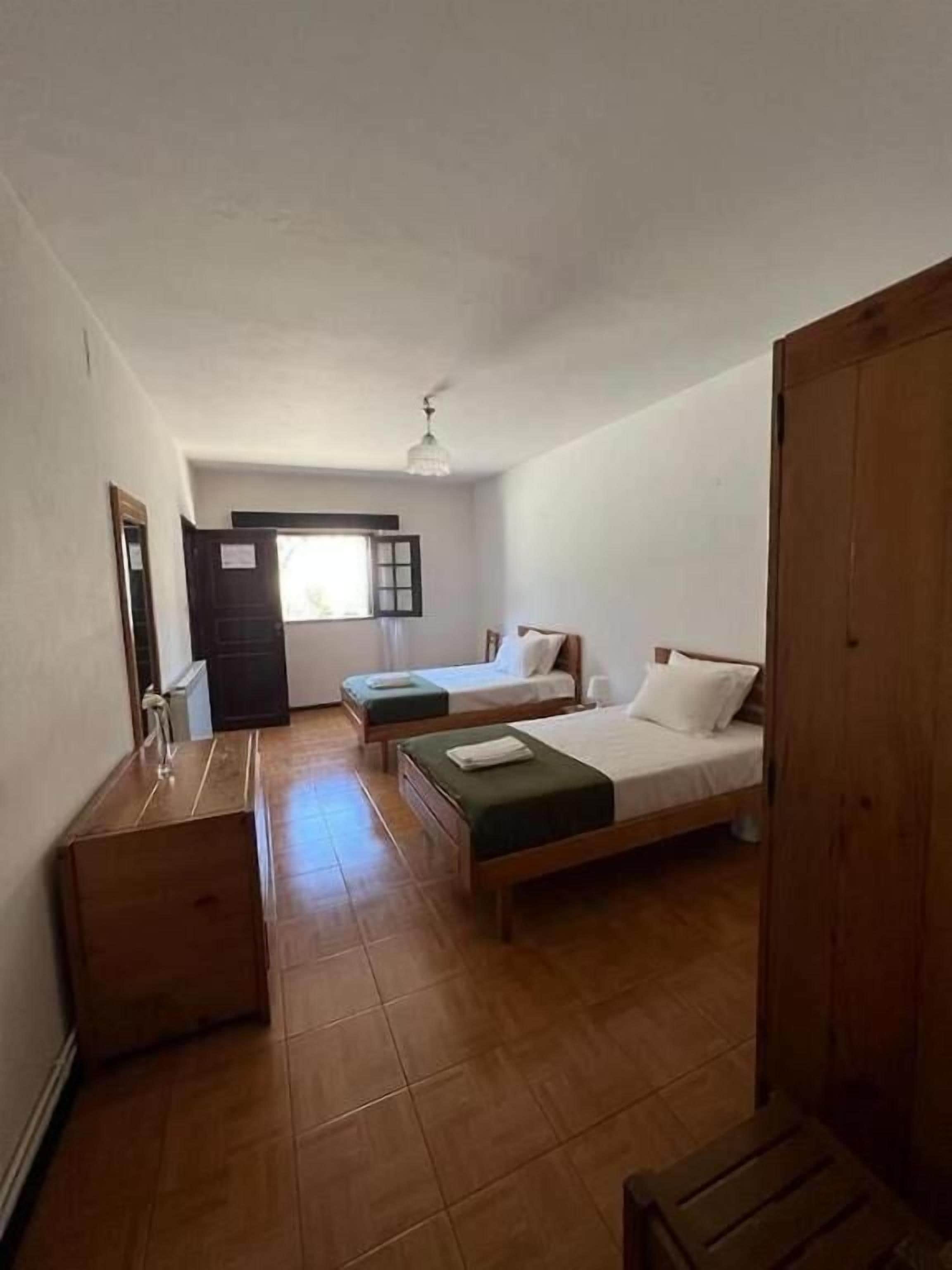 Una habitación con dos camas, un banco de madera, una mesita y un ventilador de techo.