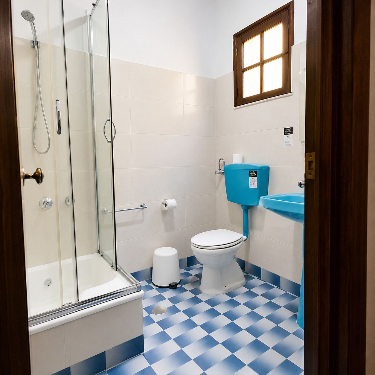 A bathroom with a glass shower enclosure, a toilet, a sink, and a checkered floor pattern.