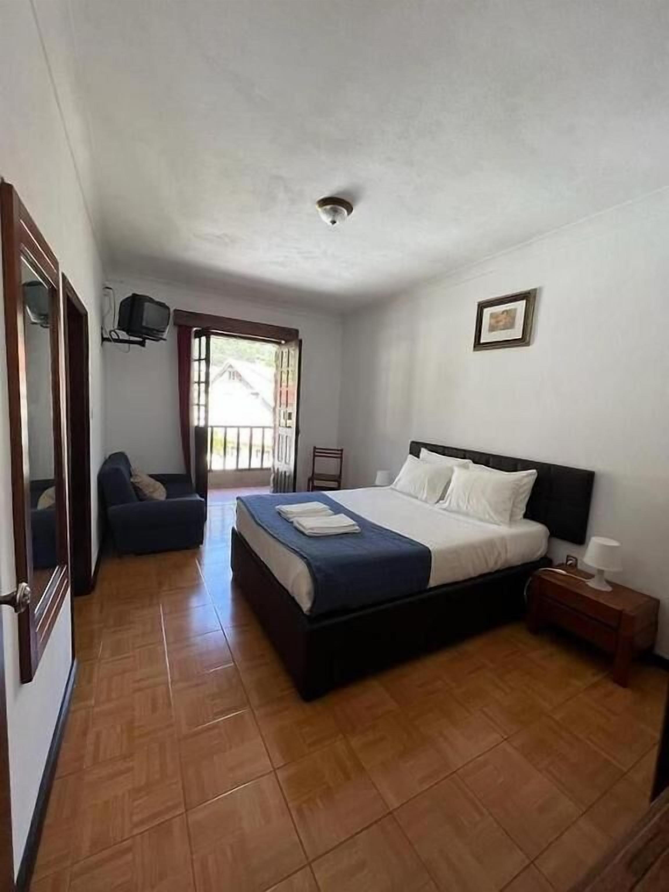 A bedroom with a bed, a chair, a nightstand, a television, and a door.