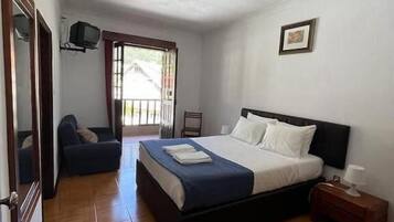 A bedroom with a bed, a chair, a nightstand, a television, and a door.