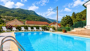 A swimming pool with lounge chairs, a mountain backdrop, and a building with a red roof.