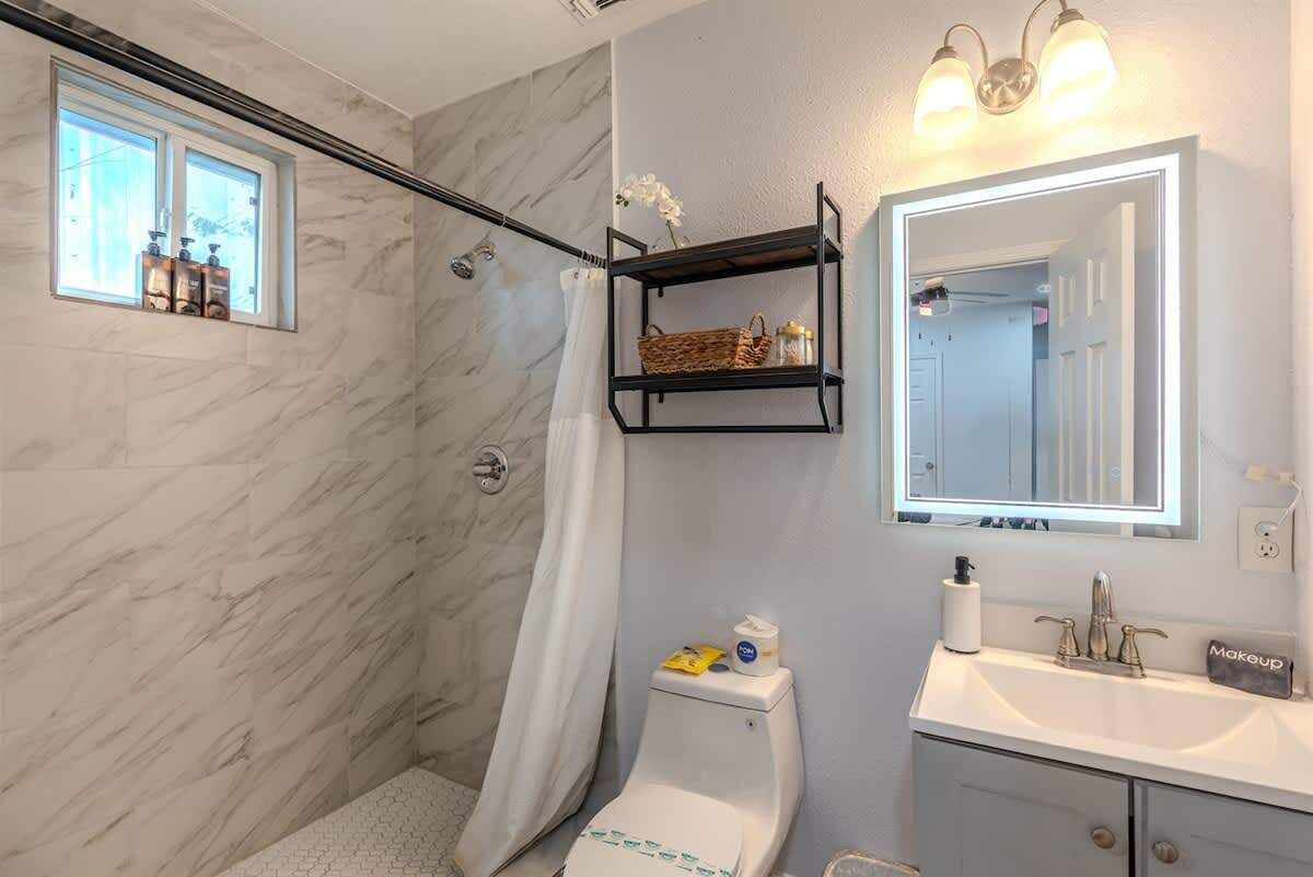 A bathroom with a marble wall, a shower, a toilet, a sink, and a shelf with toiletries.