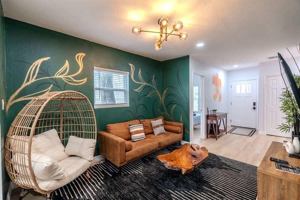 A living room with a green wall, a brown sofa, a hanging chair, and a wooden coffee table.